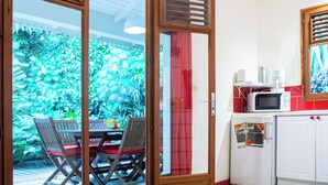 Una habitación con puerta corrediza de vidrio que da a un jardín, una mesa de comedor con sillas, un refrigerador blanco y un microondas en la encimera.