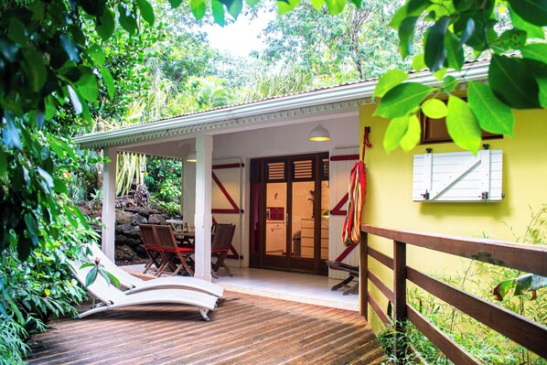 A covered outdoor area with wooden flooring, lounge chairs, and a dining table.
