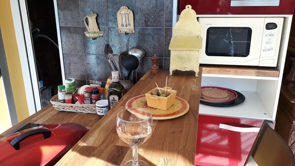 A kitchen with a microwave, a wooden table, a wine glass, and various kitchen items.