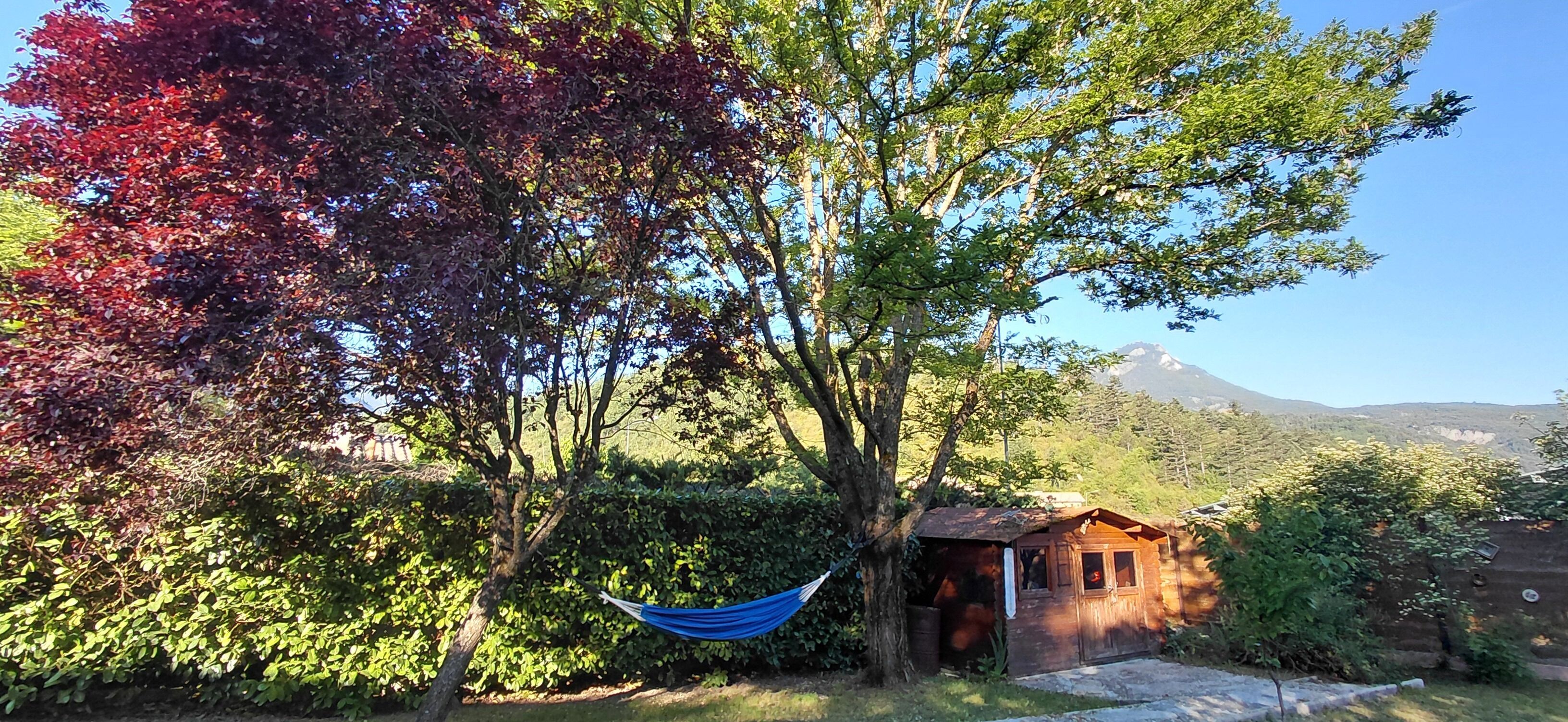 Un'amaca legata tra due alberi, una piccola struttura in legno e una montagna sullo sfondo.