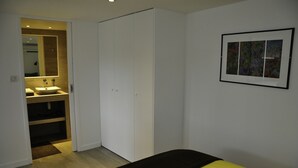 Et soveværelse med seng, skab, badeværelse med håndvask og et billede i ramme på væggen.