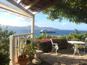 Eine Terrasse mit Steinboden, einer weißen Pergola, Blumentöpfen und einer Bank.