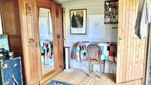 A cozy room with a wooden wardrobe, a chair, a table with a quilt, and a rug. - Gypsy Caravan and Wooden Cabin In Nature (Saint-Méard-de-Gurçon)