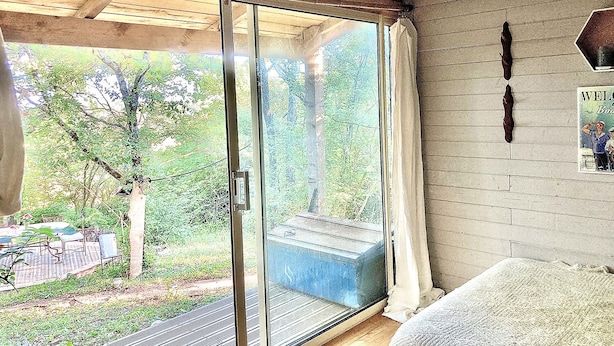 A room with a sliding glass door leading to a garden, a bed, and a welcome sign. - Gypsy Caravan and Wooden Cabin In Nature (Saint-Méard-de-Gurçon)