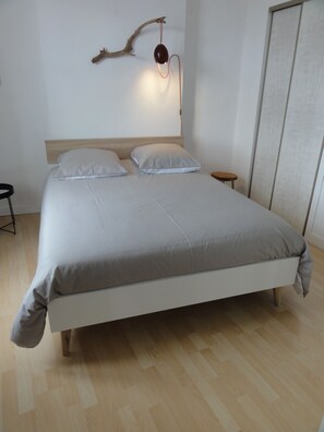 A modern bedroom with a large bed, a wooden headboard, a nightstand, and a wall-mounted light fixture. - QUAI N ° 2: BEAUTIFUL VIEW OF THE LOIRE (Saumur)