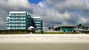 A beachfront hotel with multiple floors, a beach in the foreground, and a cloudy sky. - Amazing! Direct Oceanfront Condo - Coconut Palms Beach Resort II* Special Rates* (New Smyrna Beach)