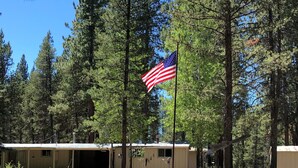 Une rangée de cabanes, avec un mât sur lequel flotte un drapeau devant, entourée d’arbres.