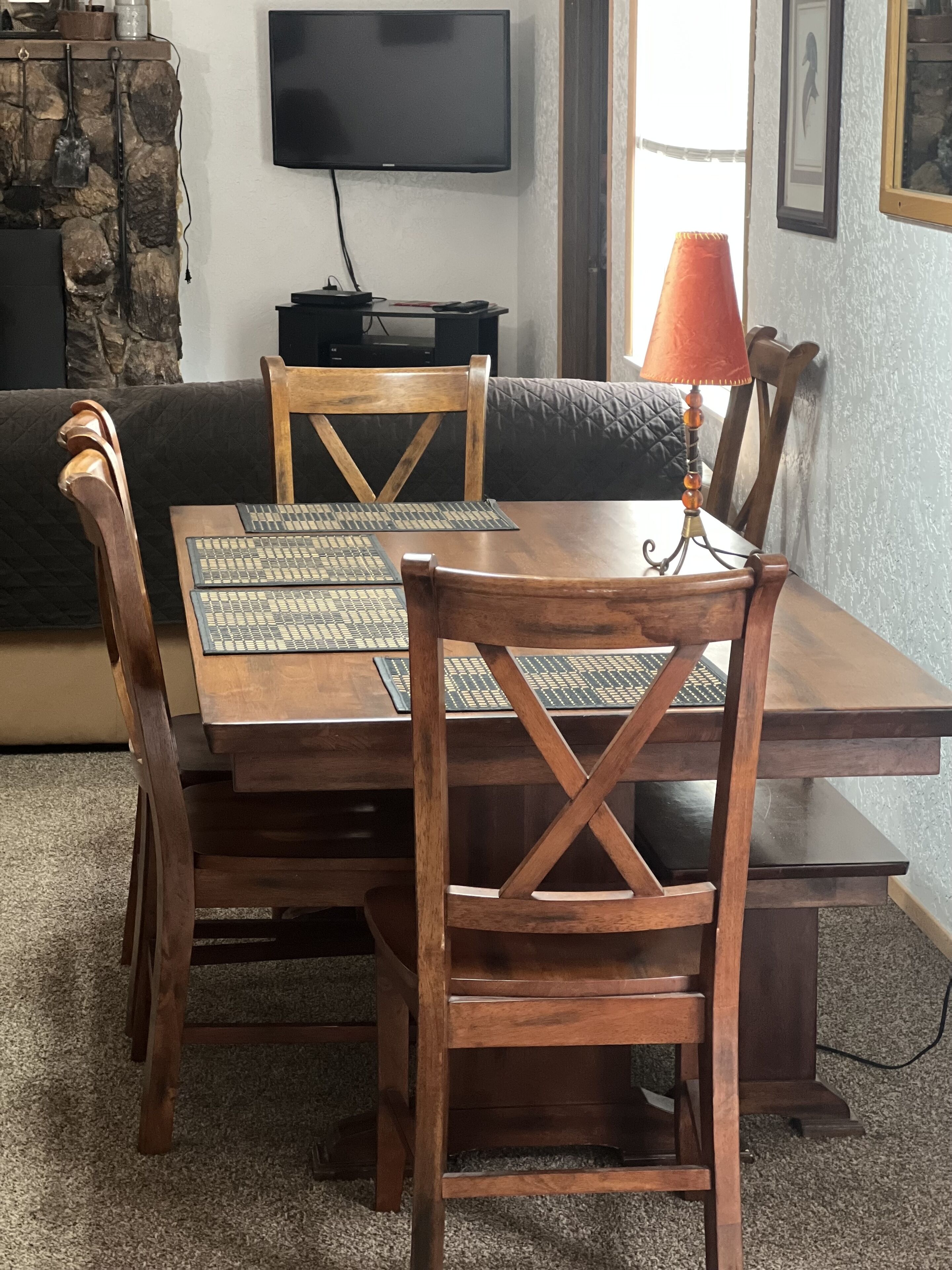 Un coin repas avec une table et des chaises en bois, un téléviseur fixé au mur et un mur en pierre qui sert d’élément décoratif.