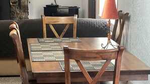 Un coin repas avec une table et des chaises en bois, un téléviseur fixé au mur et un mur en pierre qui sert d’élément décoratif.