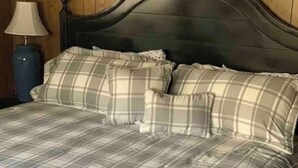 Un lit avec une couvre-lit à carreaux et des coussins assortis, une tête de lit sombre et une lampe posée sur une table de chevet en bois.