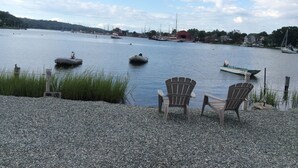 Una playa de guijarros con dos sillas de madera mirando un lago tranquilo con barcos.
