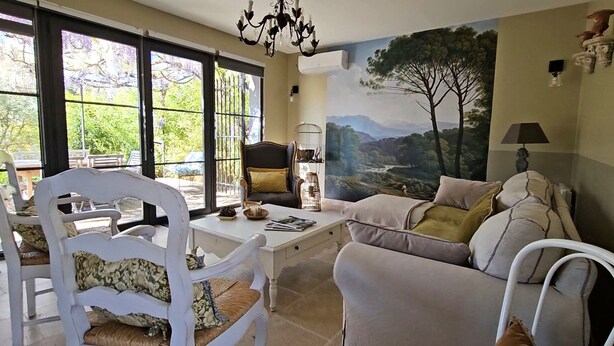 A living room with a view of a mountainous landscape through large windows, a white sofa, a white chair, and a table with decorative items.