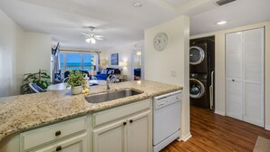 A kitchen with granite countertops, a dishwasher, and a built-in oven. There is a clock on the wall and a view of the ocean through large windows. - Beach Cottages Beachfront - Your Escape Awaits!   Sun, Secure, Family Friendly  (Indian Shores)