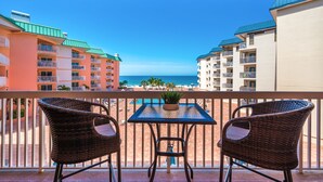 A balcony with wicker chairs and a table, overlooking a beach with buildings in the background. - Beach Cottages Beachfront - Your Escape Awaits!   Sun, Secure, Family Friendly  (Indian Shores)
