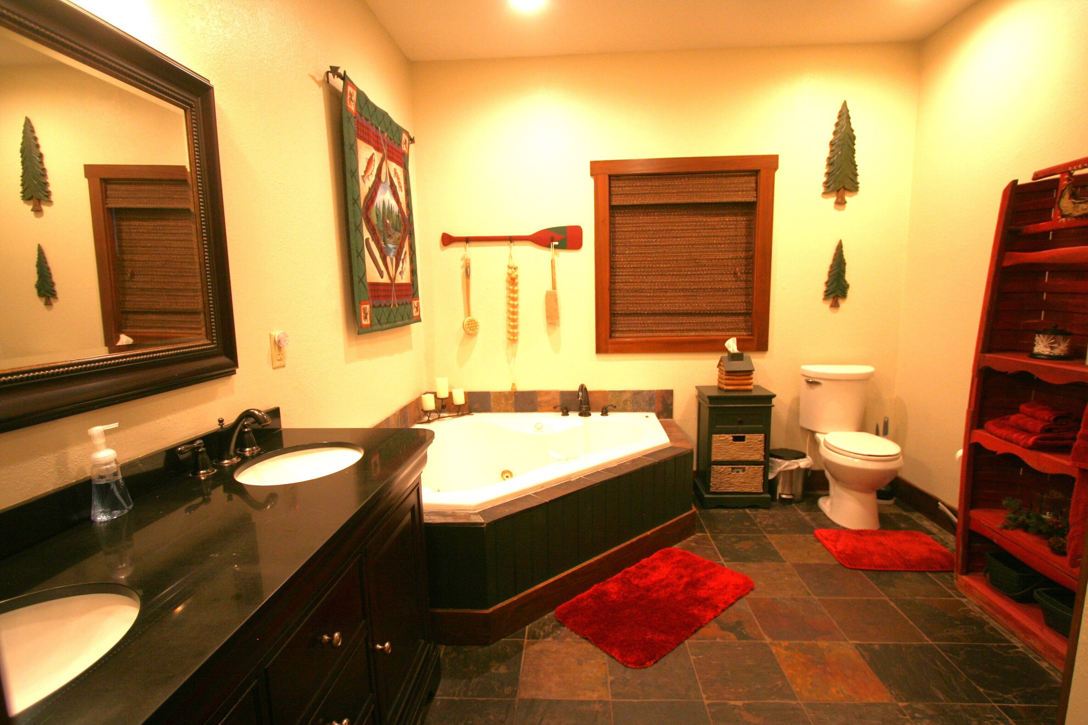 A bathroom with a large bathtub, two sinks, a toilet, and a red rug.