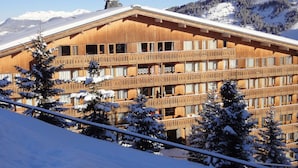 Una cabaña de madera con varios balcones, rodeada de árboles y montañas nevadas.