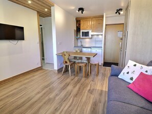 Un espacio habitable pequeño con una mesa de comedor de madera, un sofá y un televisor de pantalla plana montado en la pared.
