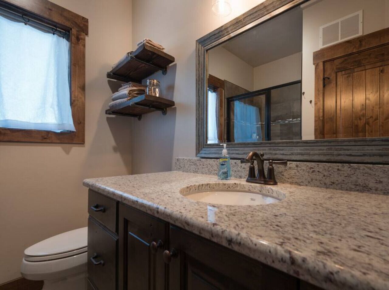 Une salle de bain avec un lavabo à vasque en granit, un meuble-lavabo en bois, un miroir et une fenêtre avec un rideau.