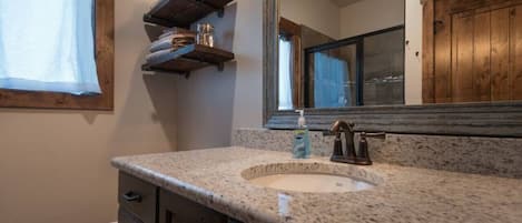 A bathroom with a granite countertop sink, a wooden vanity, a mirror, and a window with a curtain.