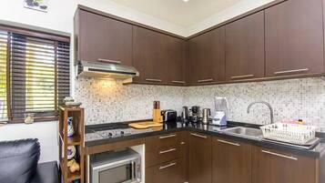 Una cocina compacta con armarios de madera oscura, un microondas, una cafetera y un lavabo.