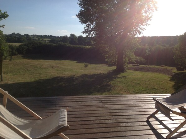 Een houten terras met twee loungestoelen, gericht op een grasveld en een boom.