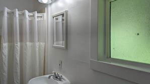 Un baño con lavamanos blanco, un espejo, una cortina de ducha y un ventanal con marco verde.