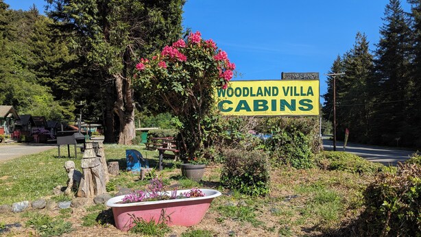 Señal de Woodland Villa Cabins con un jardín que incluye una bañera rosa y un gran árbol con flores rosas.
