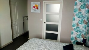 Une chambre à coucher avec un lit, une porte dotée de panneaux en verre dépoli, un tableau accroché au mur et un rideau orné d’un motif de feuilles.
