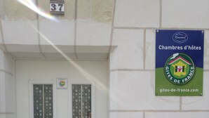 Une porte blanche avec une fenêtre, une plaque portant le numéro « 37 » au-dessus, et une enseigne sur le mur faisant de la publicité pour les « chambres d’hôtes » et les « gîtes de France ».