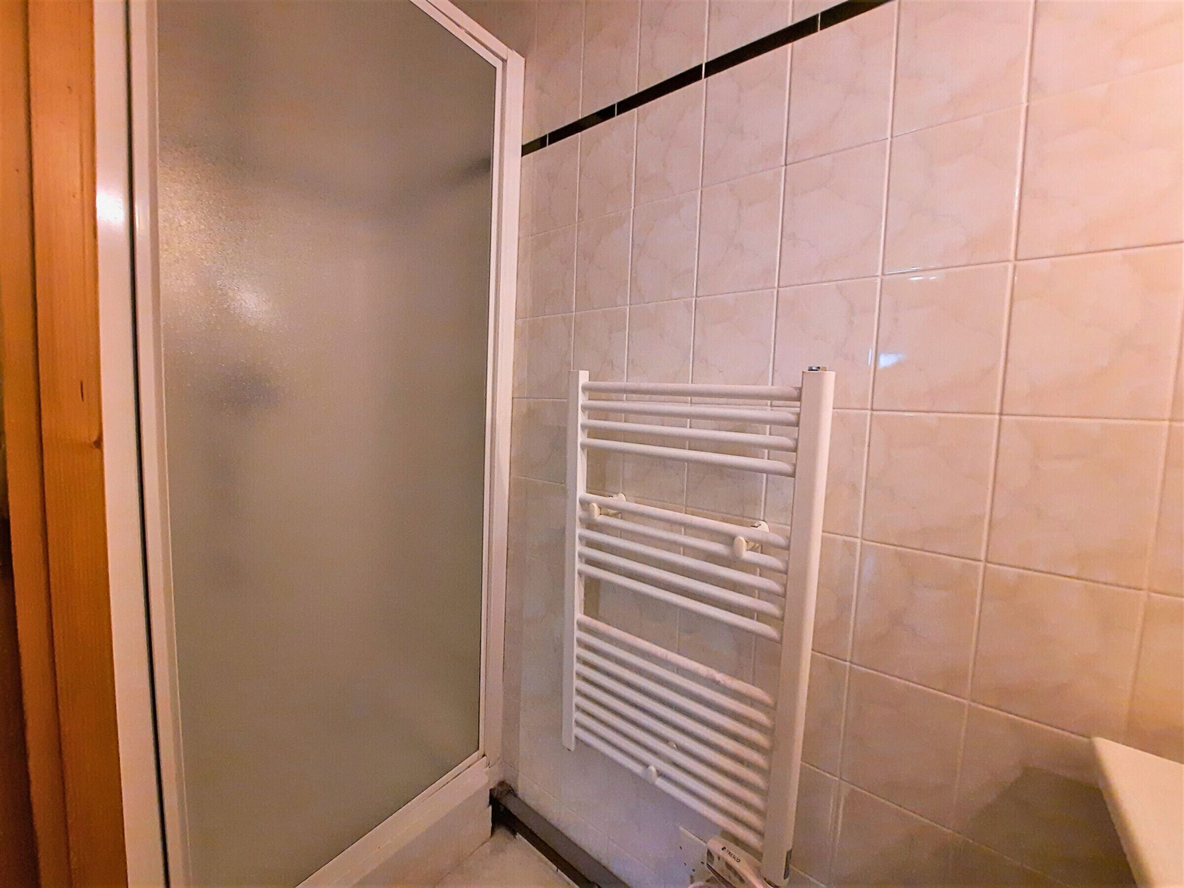 A bathroom with a white tiled wall, a white towel rack, and a shower area.