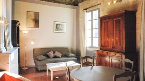 Una sala de estar acogedora con un sofá, una mesa de centro y una mesa de comedor con sillas. Se observa un aparador de madera y una ventana con cortinas.