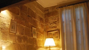 Una habitación acogedora con pared de piedra, una cama con ropa de cama floral, dos lámparas de noche y una cortina.