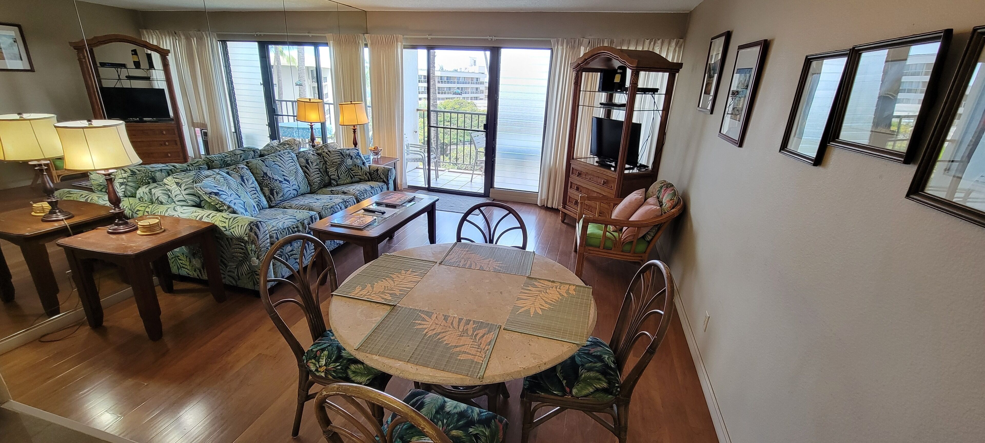 Un salon avec un canapé, une table à manger avec des chaises, un téléviseur et un balcon avec des rideaux.