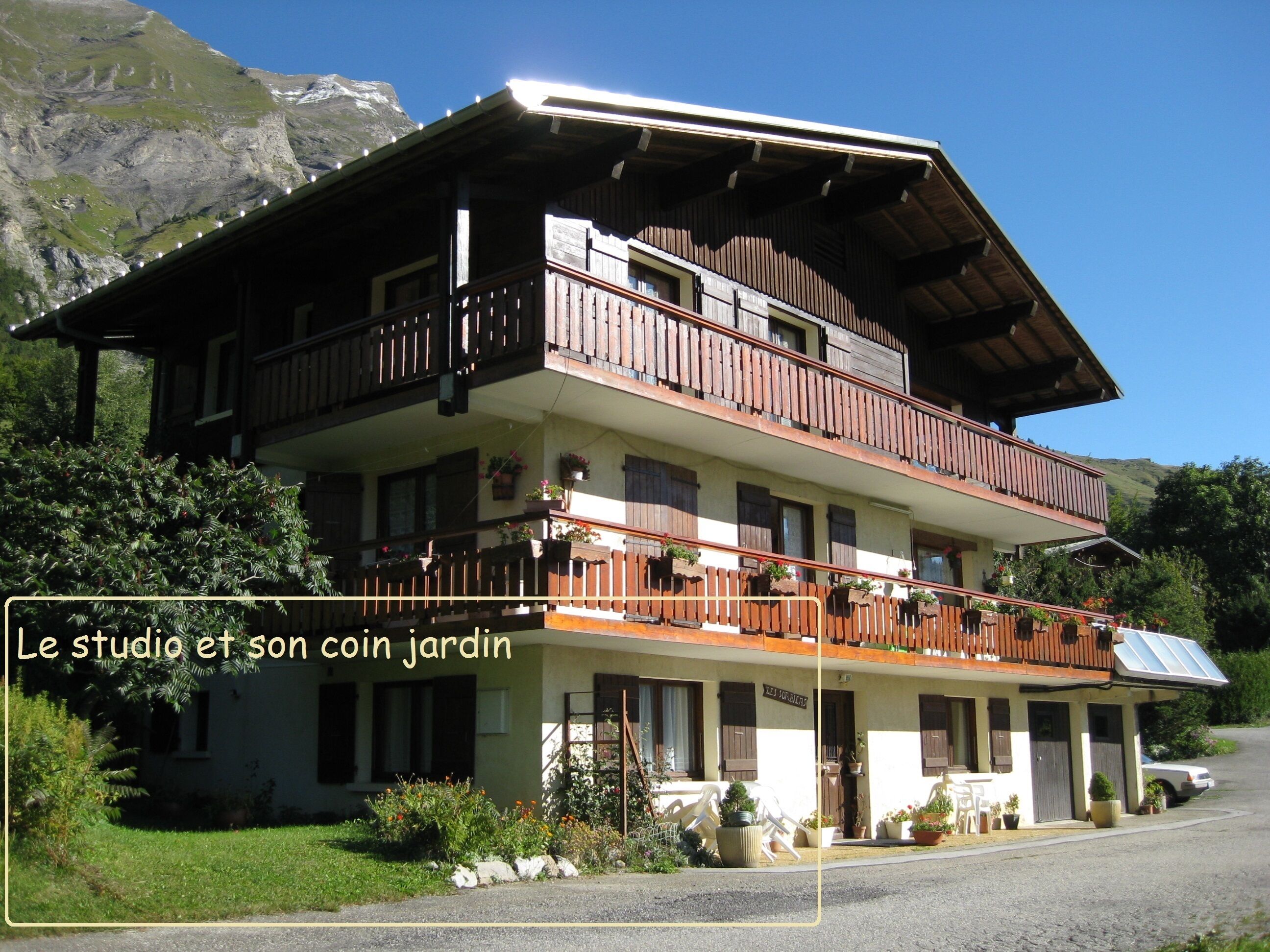 A two-story building with a balcony, surrounded by greenery and mountains.