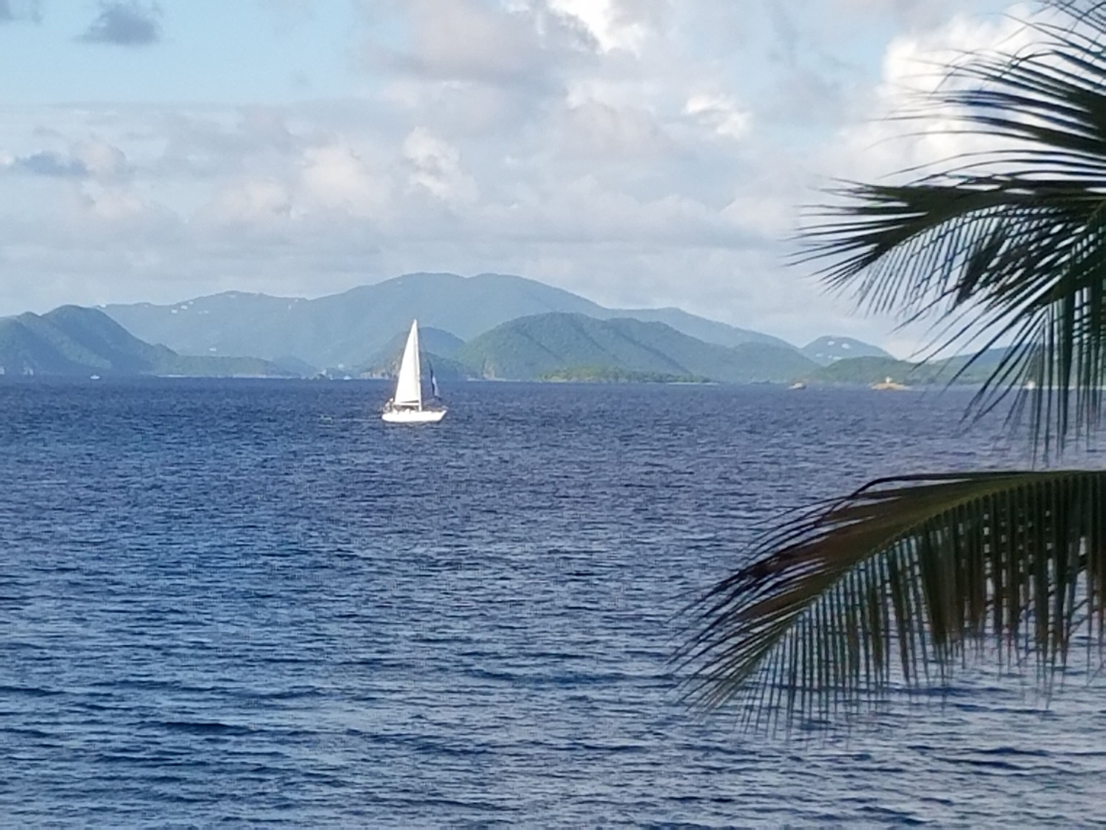 Un velero en aguas tranquilas, con montañas al fondo.