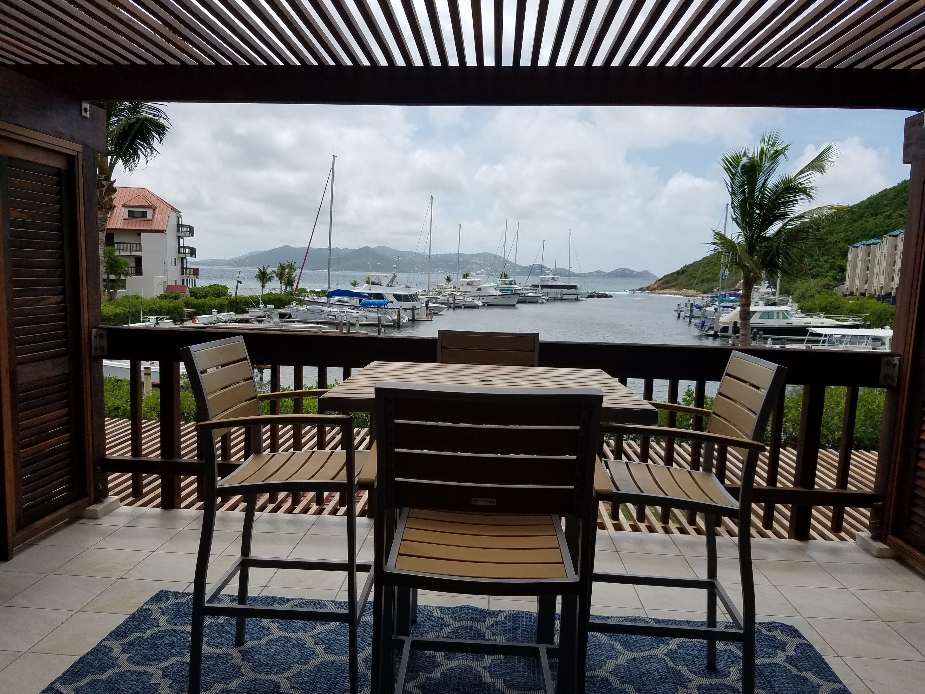 Un espace extérieur abrité, aménagé avec des sièges, et offrant une vue sur un port de plaisance et des bateaux.