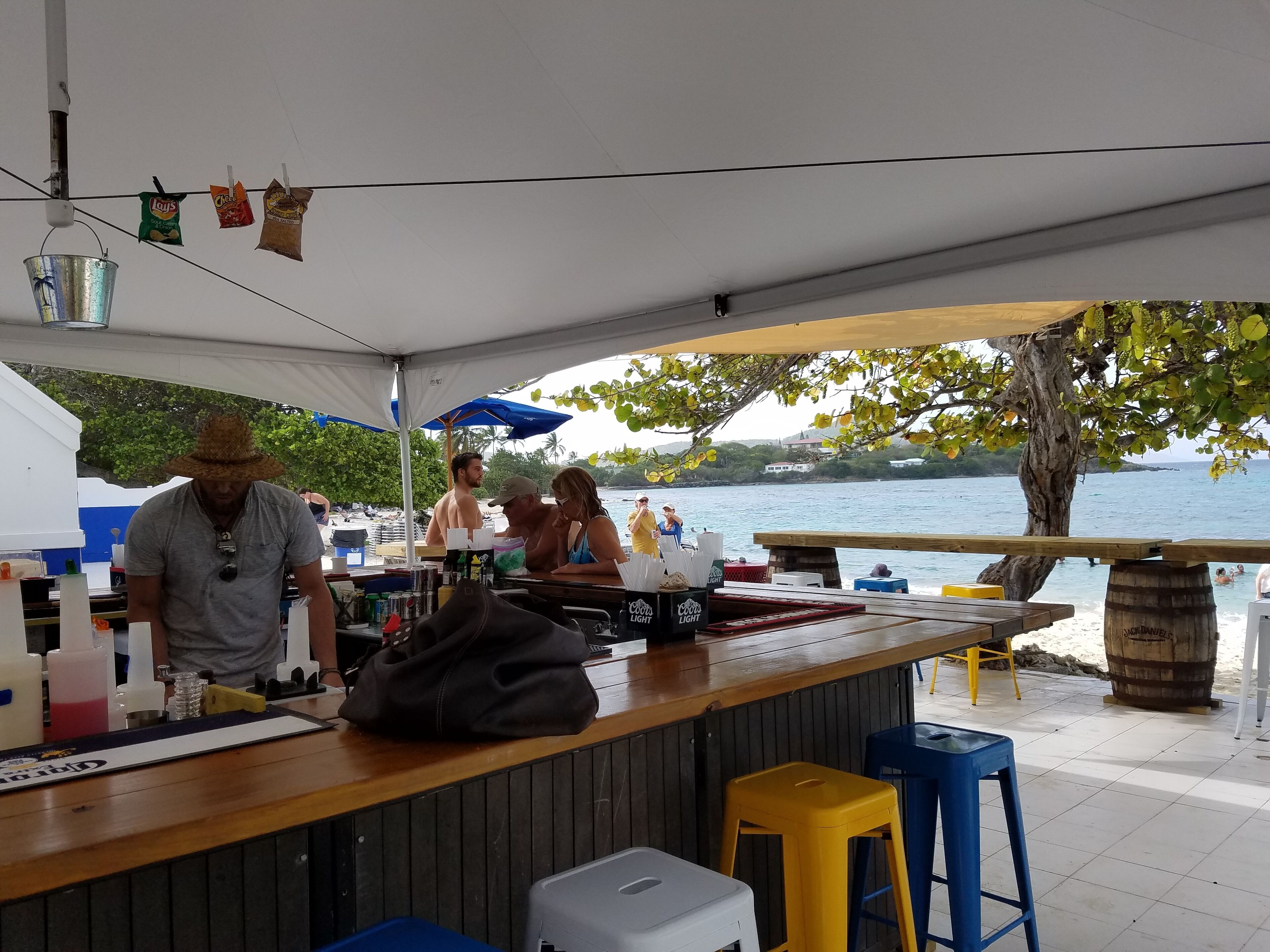 A beachside bar with a wooden counter, a cooler, and a metal bucket.