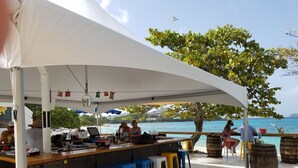A beachside bar with a white canopy, wooden bar counter, and colorful stools. - Welcome to Paradise! (St Thomas)
