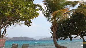 A beach with three metal chairs, a palm tree, and a view of the ocean. - Welcome to Paradise! (St Thomas)