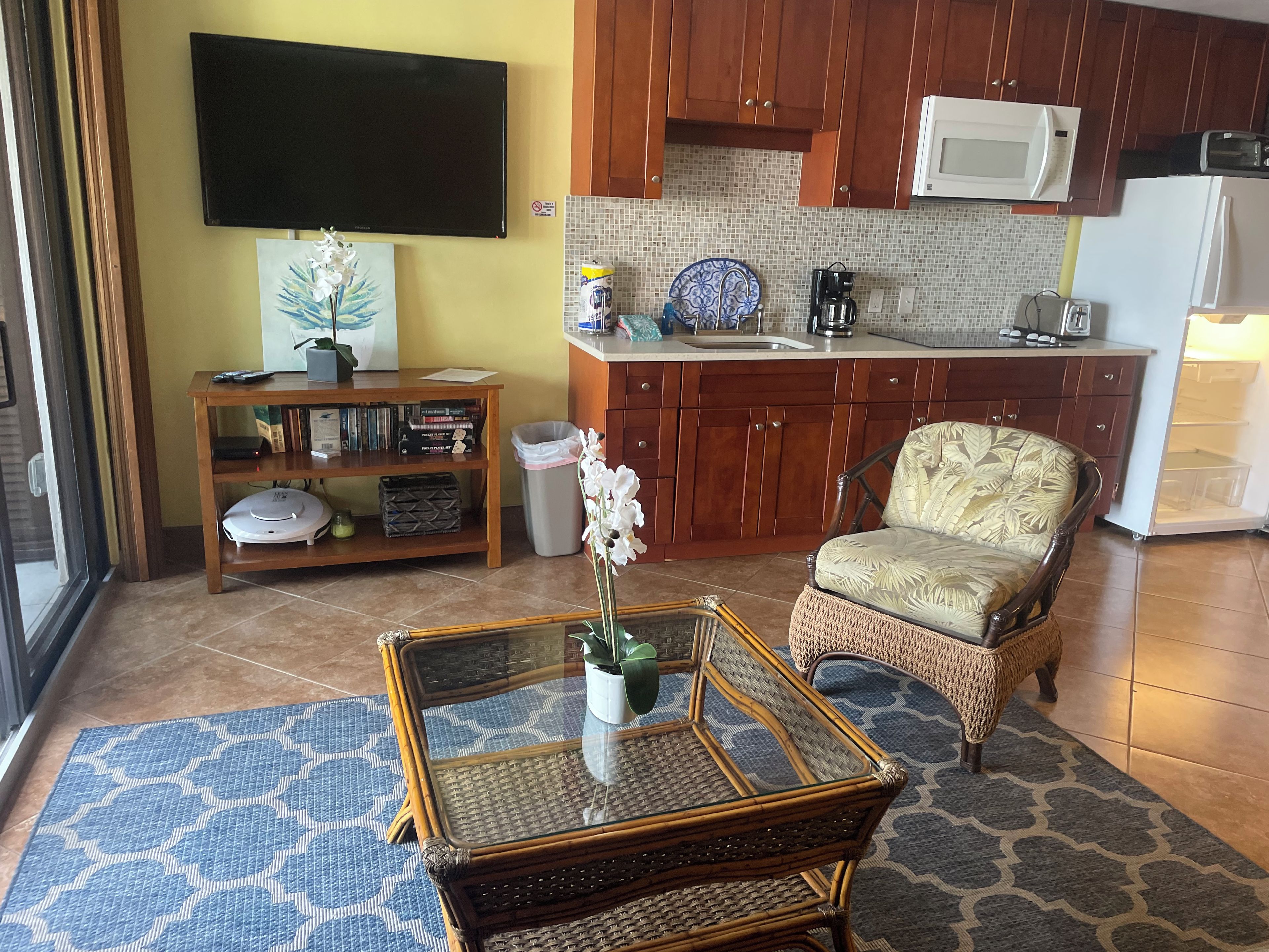 Ein Wohnzimmer mit Fernseher, Bücherregal, Korbsessel und Glastisch.