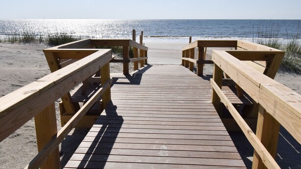 Una pasarela de madera que lleva a una playa arenosa con el océano al fondo.