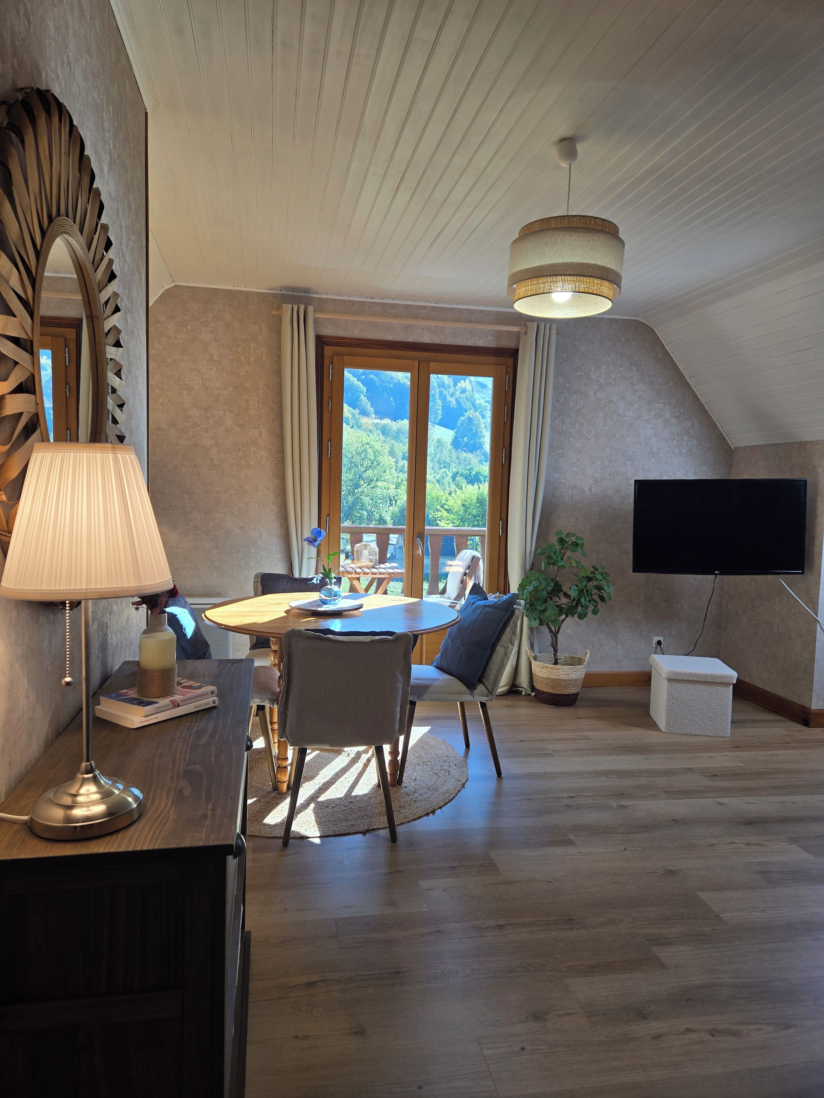 A dining area with a table, chairs, a lamp, a TV, and a view of the outdoors.