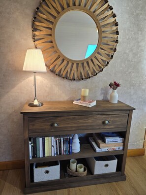 A wooden console table with a mirror, a lamp, a vase with flowers, and bookshelves. - Your charming getaway in the heart of the Pyrenees (Luz-Saint-Sauveur)