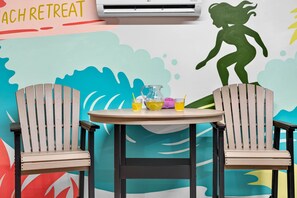 Un cuarto con temática playera, con dos sillas Adirondack, una mesa con bebidas y un mural con la silueta de una persona.