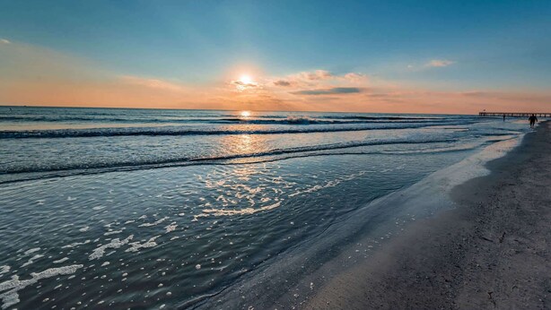 Ein Strand mit Wellen, einem Steg und einem Sonnenuntergang.