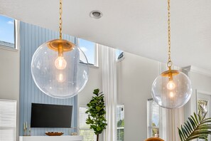 Ein modernes Wohnzimmer mit zwei kugelförmigen Pendelleuchten, einem Flachbildfernseher und einer großen Topfpflanze.