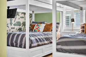 Una cama litera con una patineta y un adhesivo de palmera, un cojín con la inscripción 'SUN SURF SEA SALT SAND' y una lámpara de noche.