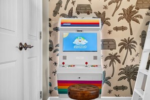 Een kamer met een witte deur, een witte kast met een kleurrijk gestreept onderstuk, een klein houten krukje en een muur met een tropisch patroon.