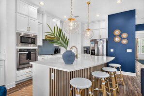 Una cocina moderna con armarios blancos, electrodomésticos de acero inoxidable, una isla central con taburetes y una pared de acento azul.