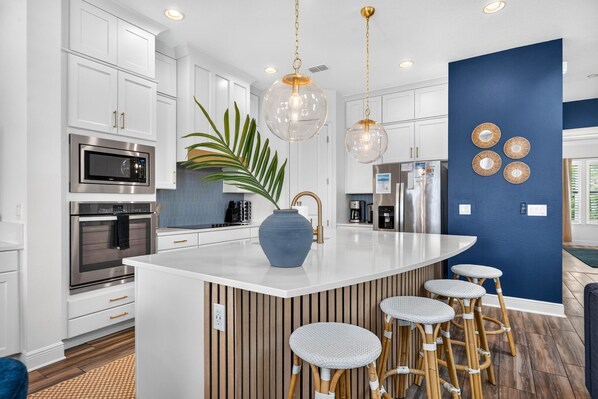 A modern kitchen with white cabinetry, stainless steel appliances, a central island with stools, and a blue accent wall.